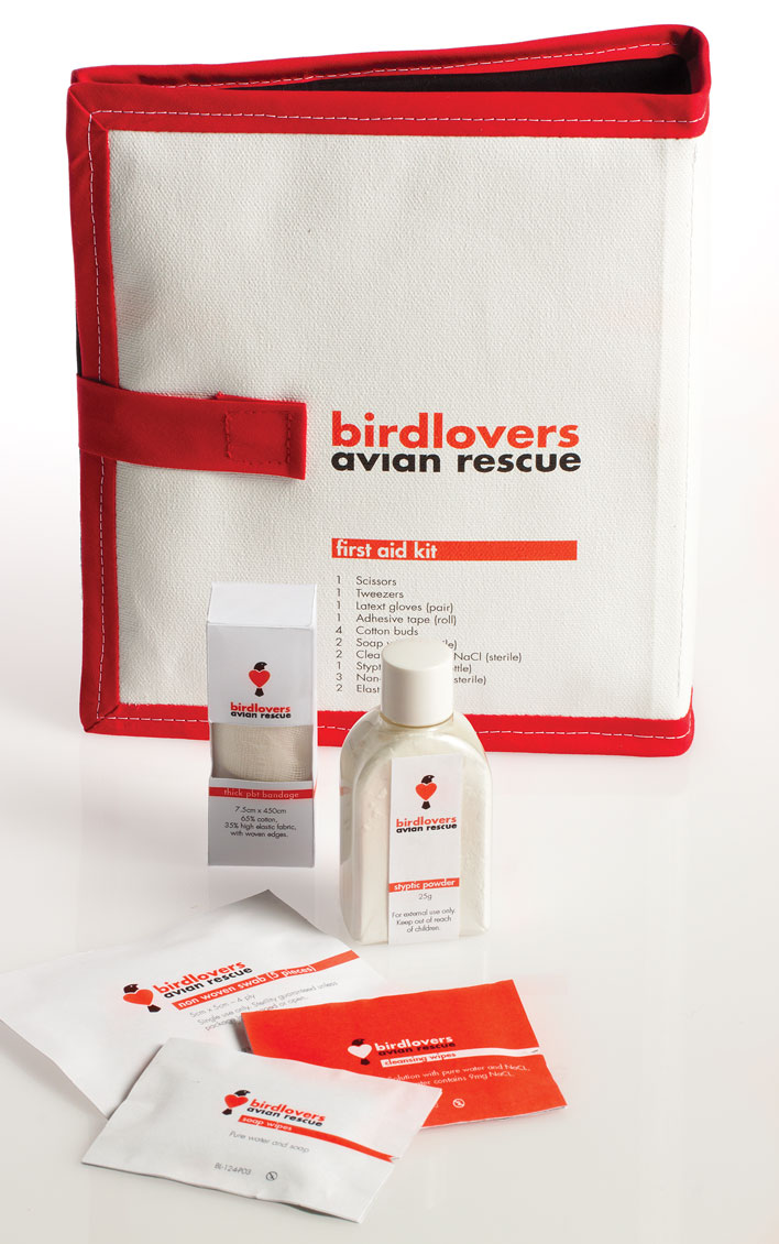 The first-aid kit for Birdlovers Avian Rescue - a canvas wallet, with red trim and printed with the brand's logo. In front of the first-aid kit sits some of the contents including packaged bandages, a bottle of styptic powder, swabs and cleansing wipes all packaged with the brand's logo and colours in black, white and red.