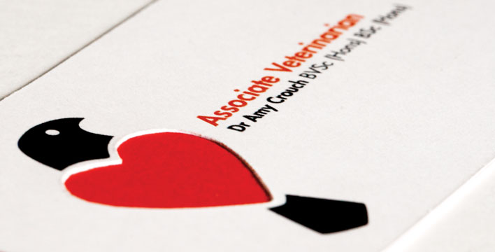 The business card is layered with a thin red paper sandwiched between two white cards. The card back features the logo's bird element with heart-shaped wings cut out to reveal the red layer.