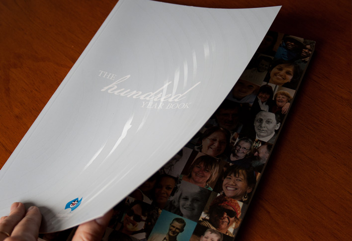 Cover of The Hundred Year Book which features a matt cello glaze with a glossy spot uv treatment representing tree rings, symbolising the years of history of Frontier Services. Lifting the cover reveals a collage of happy faces from photos taken throughout the 100 years of service.