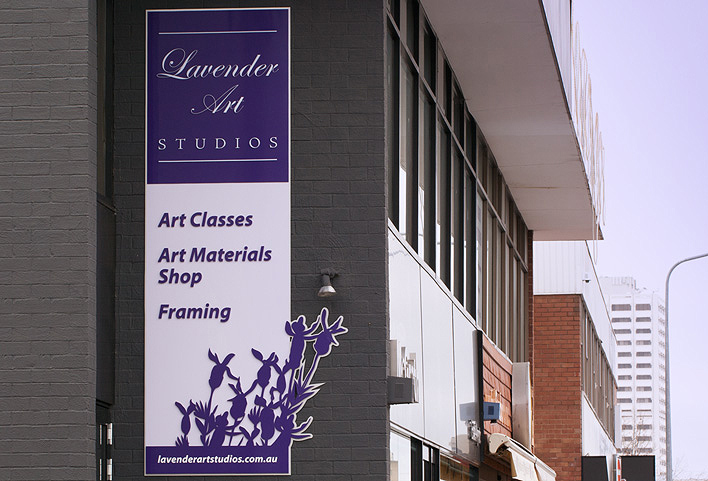 The purple and pale lavender shop sign made from smooth acrylic features the words Lavender Art Studios,  art classes, art materials shop and framing, and the studio's website. The sign also features stylised sprigs of lavender.
